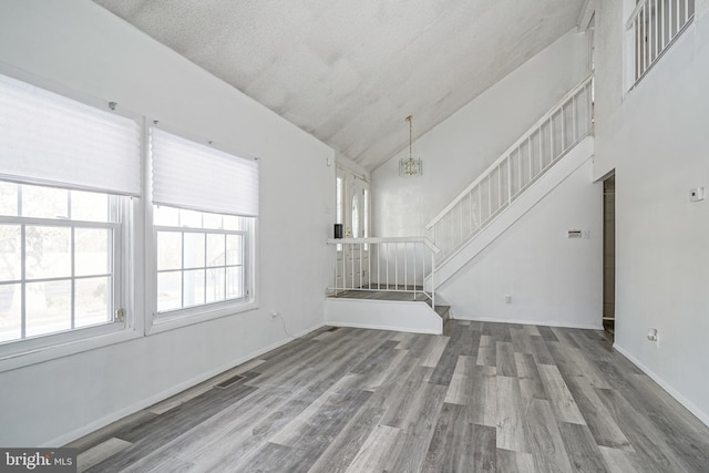 unfurnished living room featuring vaulted ceiling, an inviting chandelier, a textured ceiling, and hardwood / wood-style floors