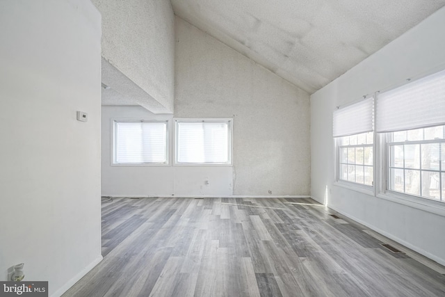 spare room featuring high vaulted ceiling, a textured ceiling, and light hardwood / wood-style floors