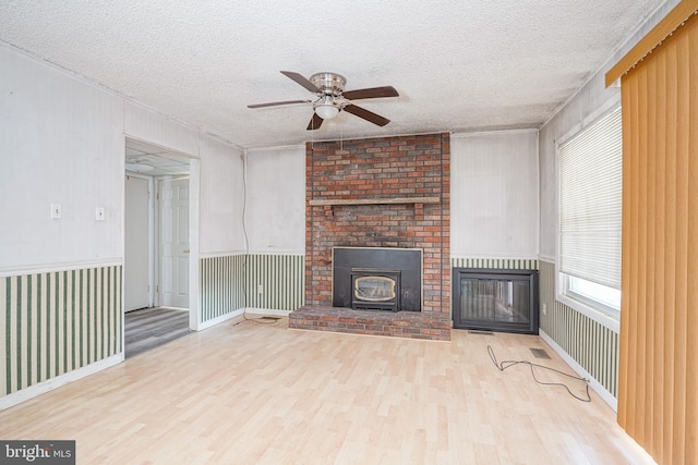 unfurnished living room with ceiling fan, a textured ceiling, light hardwood / wood-style flooring, and a brick fireplace