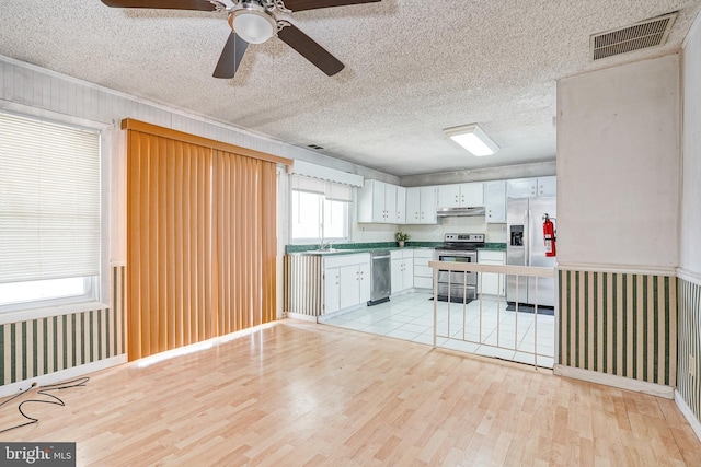 kitchen with a textured ceiling, white cabinets, appliances with stainless steel finishes, ceiling fan, and light hardwood / wood-style flooring