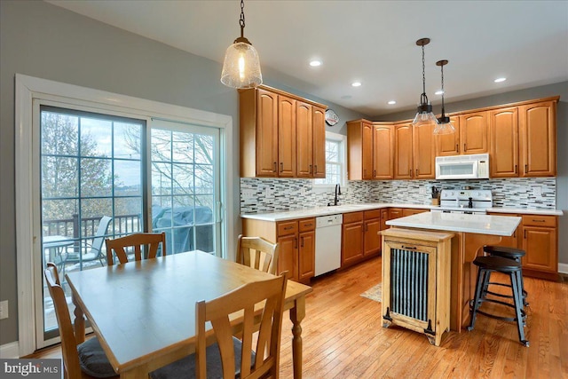 kitchen with light wood-type flooring, white appliances, sink, a center island, and hanging light fixtures