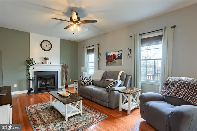 living room with ceiling fan, a large fireplace, and light hardwood / wood-style floors