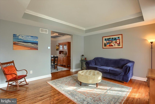 living room featuring hardwood / wood-style flooring, ornamental molding, and a tray ceiling