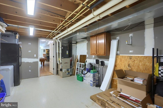 basement featuring wooden walls, black fridge, fridge, and heating unit