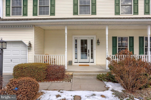 snow covered property entrance with covered porch and a garage