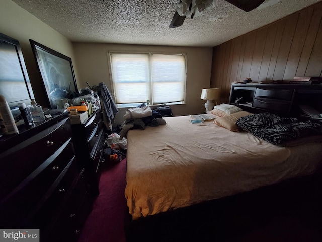 bedroom featuring a textured ceiling, ceiling fan, and wood walls