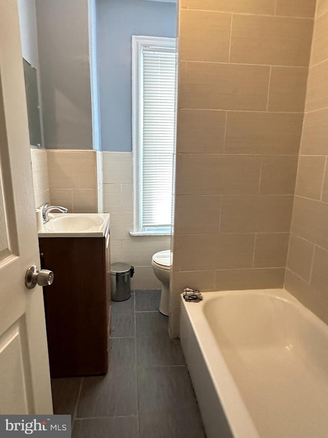 bathroom featuring tile patterned floors, vanity, toilet, and tile walls