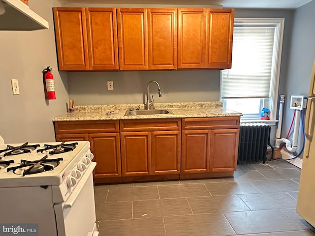 kitchen featuring light stone countertops, radiator heating unit, white gas range, and sink