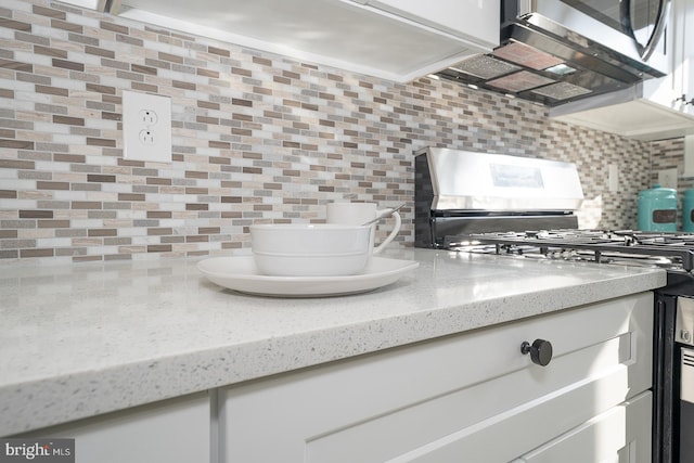 interior space featuring gas range oven, backsplash, white cabinetry, and light stone counters