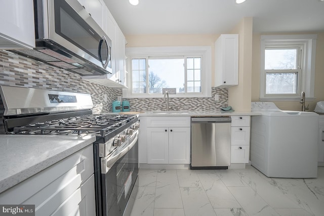 kitchen featuring sink, decorative backsplash, washer / dryer, white cabinetry, and stainless steel appliances