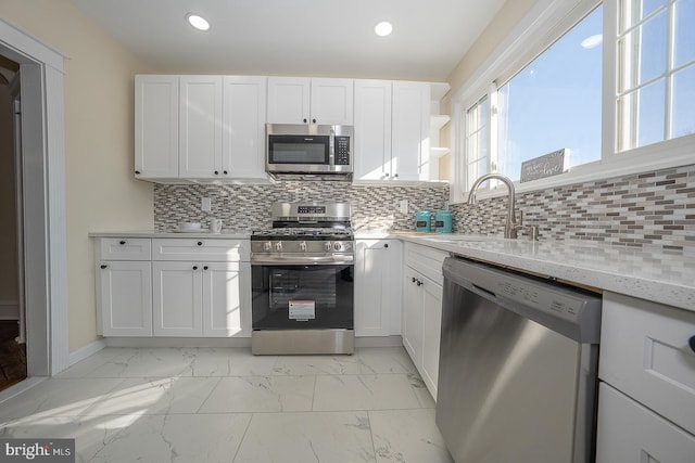 kitchen featuring light stone counters, stainless steel appliances, white cabinetry, and sink