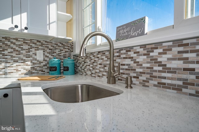 room details featuring backsplash, light stone countertops, sink, and white cabinetry