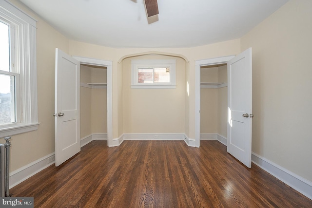 unfurnished bedroom featuring multiple windows, dark hardwood / wood-style floors, ceiling fan, and multiple closets