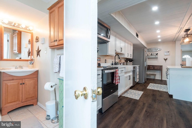 kitchen featuring white cabinetry, sink, wood-type flooring, light brown cabinetry, and appliances with stainless steel finishes