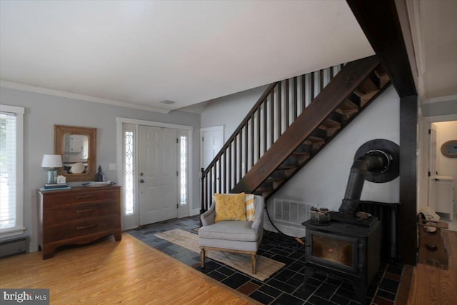 foyer featuring hardwood / wood-style floors, a wood stove, baseboard heating, and ornamental molding