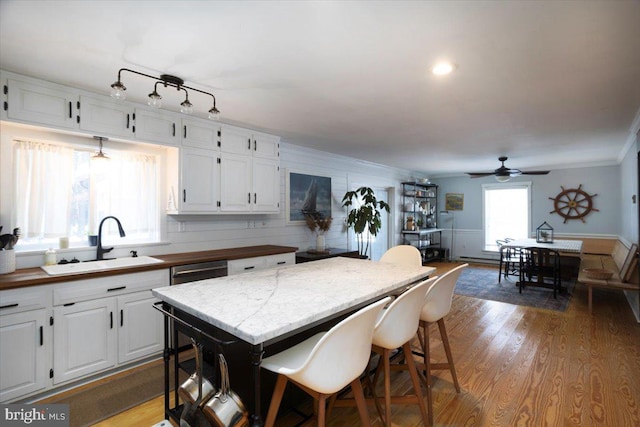 kitchen featuring ceiling fan, sink, light wood-type flooring, white cabinets, and ornamental molding