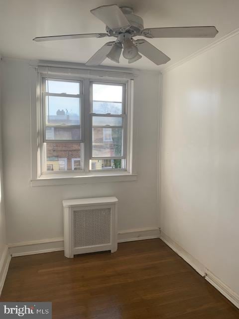 spare room with dark hardwood / wood-style flooring, radiator, ornamental molding, and ceiling fan