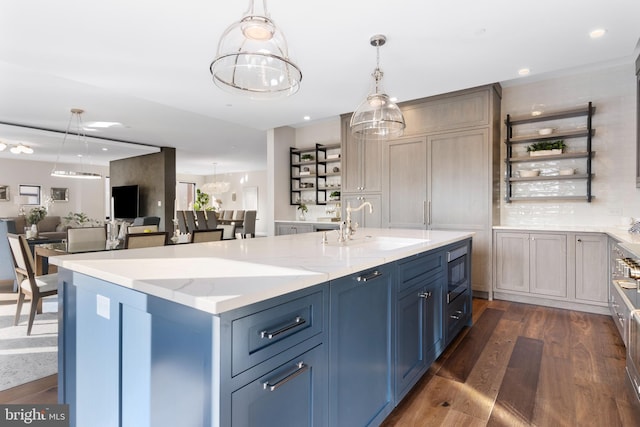 kitchen featuring a center island with sink, dark wood-type flooring, open floor plan, a sink, and light stone countertops