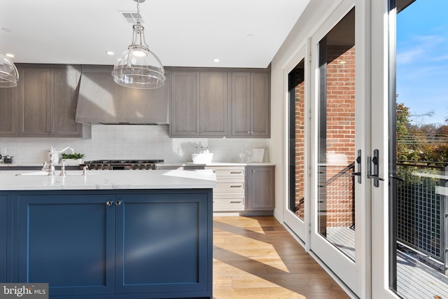 kitchen with visible vents, decorative backsplash, wall chimney exhaust hood, light wood-style floors, and a sink