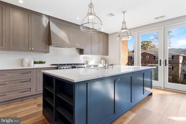 kitchen with wall chimney exhaust hood, light wood-type flooring, a sink, and visible vents