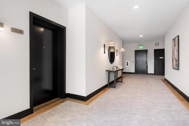 hall featuring baseboards, visible vents, and light wood-style flooring