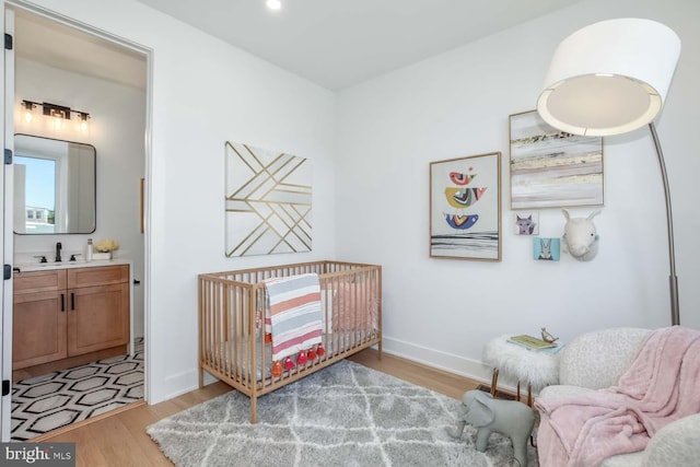 bedroom with light hardwood / wood-style flooring, a nursery area, and sink