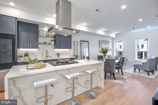 kitchen featuring stainless steel gas stovetop, a kitchen island, light wood-type flooring, island range hood, and a kitchen bar