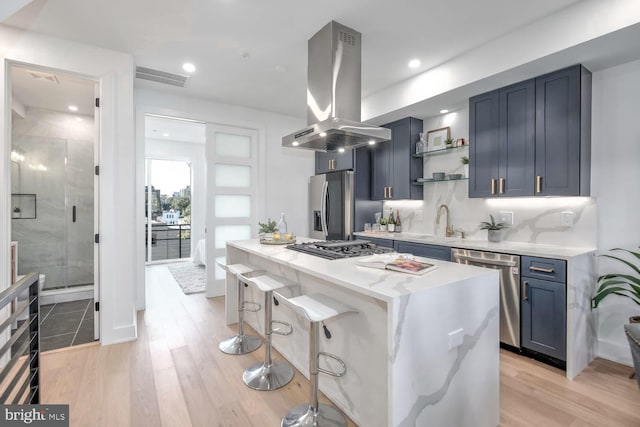 kitchen with blue cabinets, a kitchen island, light hardwood / wood-style floors, island range hood, and stainless steel appliances