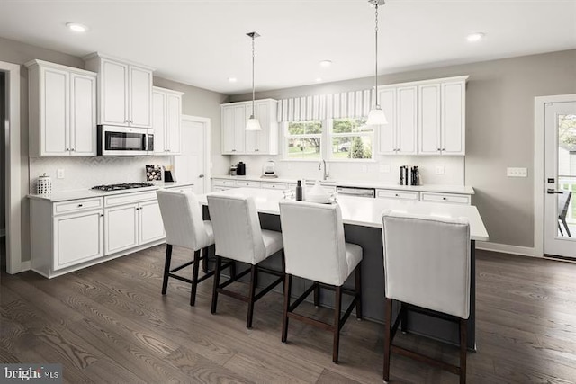 kitchen with stainless steel appliances, a kitchen island with sink, dark wood-type flooring, pendant lighting, and white cabinets