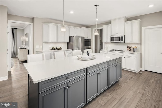 kitchen with gray cabinetry, white cabinetry, hanging light fixtures, a kitchen island, and appliances with stainless steel finishes