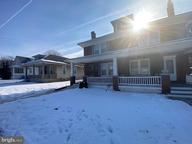 snow covered rear of property featuring covered porch