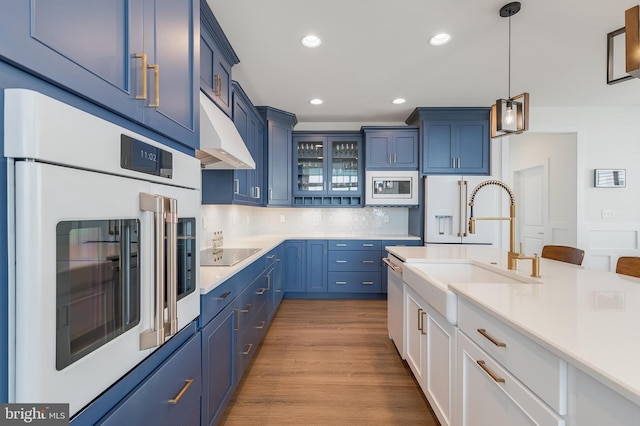 kitchen with white microwave, oven, hanging light fixtures, blue cabinetry, and tasteful backsplash