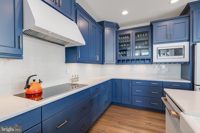 kitchen featuring backsplash, black electric cooktop, blue cabinets, built in microwave, and hardwood / wood-style floors