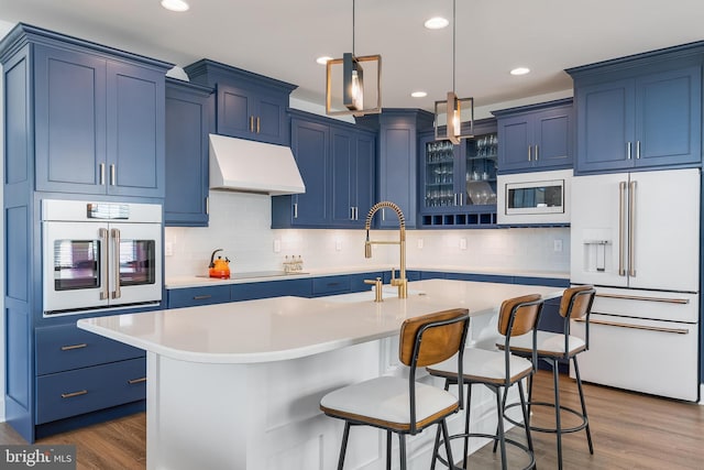 kitchen with wood-type flooring, white appliances, a center island with sink, and blue cabinets