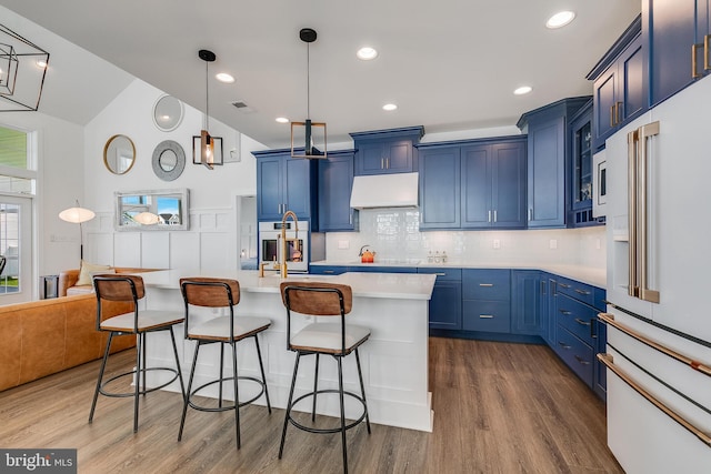 kitchen with dark hardwood / wood-style flooring, high end fridge, blue cabinetry, a center island with sink, and hanging light fixtures