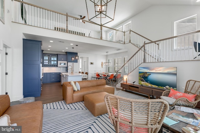 living room with a towering ceiling, an inviting chandelier, dark wood-type flooring, and sink