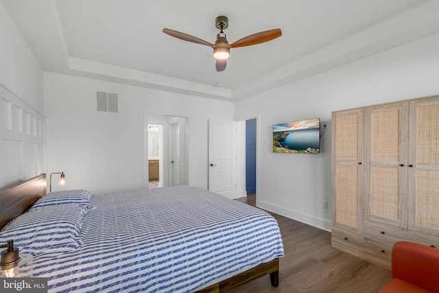 bedroom featuring ceiling fan, a raised ceiling, dark wood-type flooring, and ensuite bath