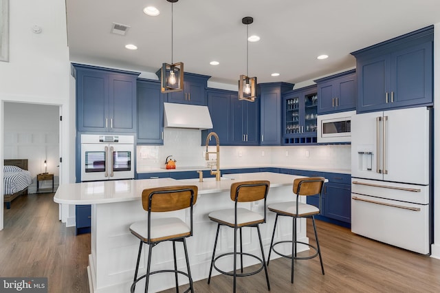 kitchen featuring wall oven, high end white fridge, blue cabinets, built in microwave, and a center island with sink