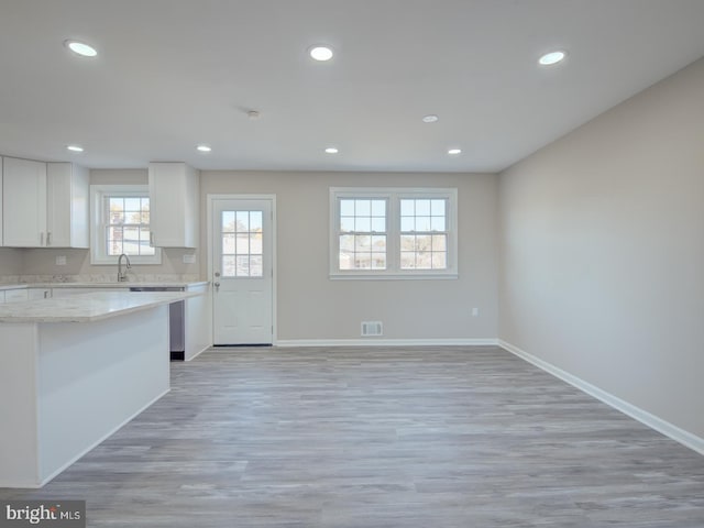 kitchen with white cabinetry, light hardwood / wood-style flooring, light stone counters, and sink