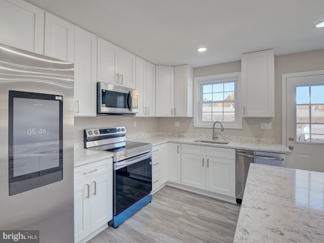 kitchen with light stone countertops, appliances with stainless steel finishes, sink, light hardwood / wood-style flooring, and white cabinets