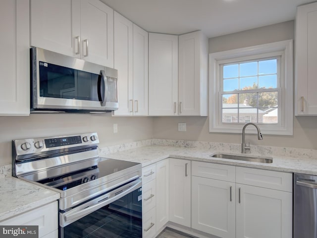 kitchen with light stone countertops, stainless steel appliances, white cabinetry, and sink