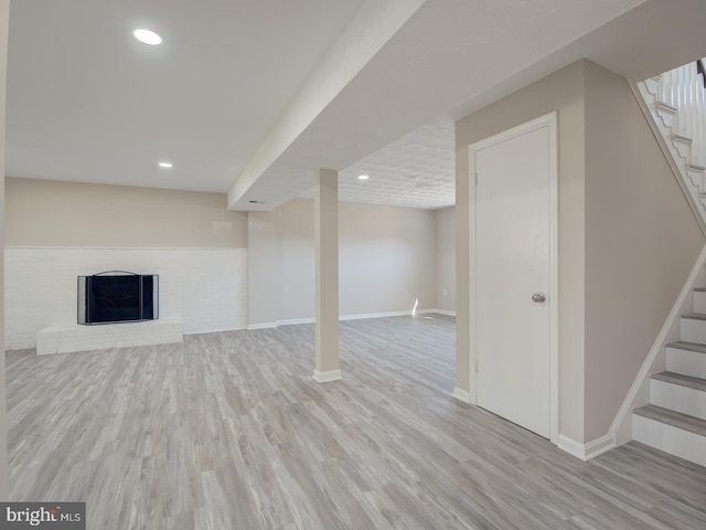 basement featuring light hardwood / wood-style flooring and a brick fireplace