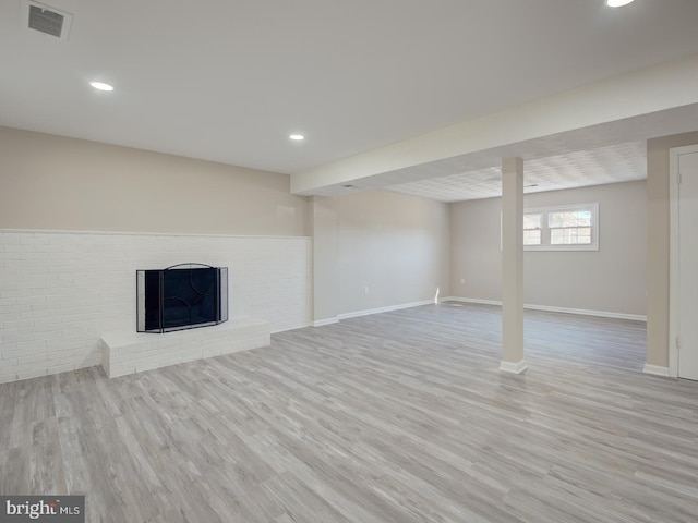 basement featuring a brick fireplace and light hardwood / wood-style flooring