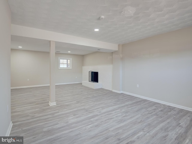 basement with a brick fireplace and light wood-type flooring