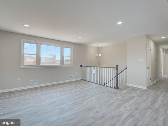 spare room with a chandelier and light wood-type flooring