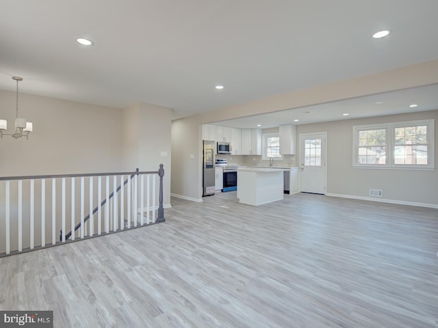 unfurnished living room featuring light wood-type flooring, sink, and an inviting chandelier