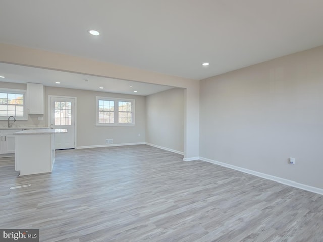 unfurnished living room with plenty of natural light, light wood-type flooring, and sink