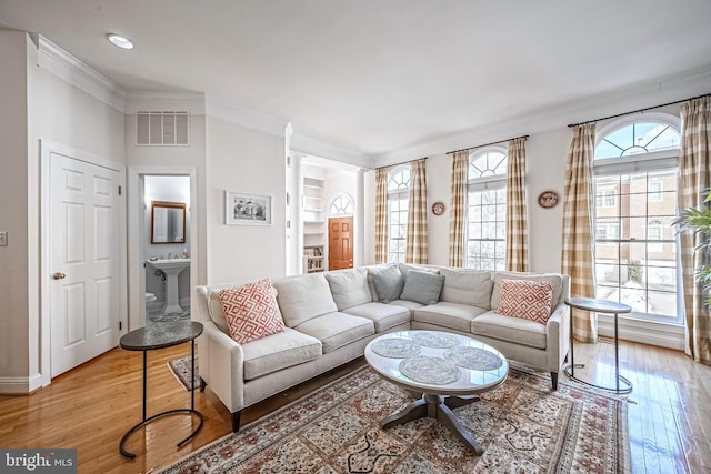 living room featuring light wood-type flooring, crown molding, and decorative columns