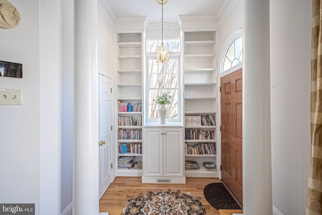 entrance foyer featuring light hardwood / wood-style floors, ornamental molding, and a notable chandelier