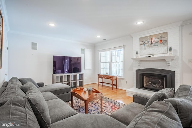 living room with a large fireplace, ornamental molding, and light hardwood / wood-style flooring